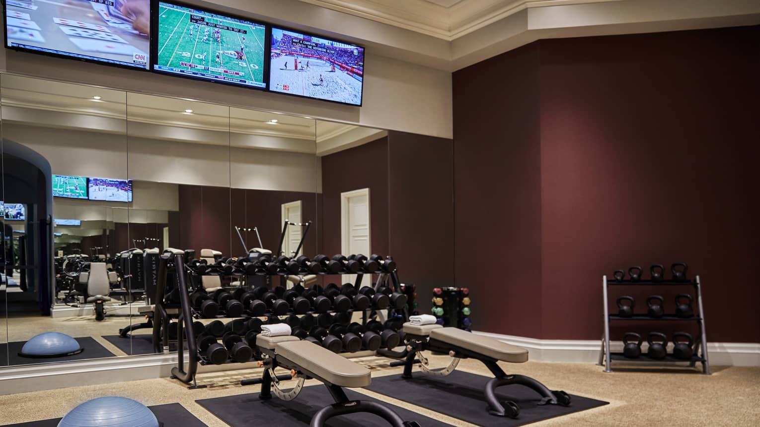 Racks of hand weights, kettlebells by Fitness Centre mirror wall under TVs