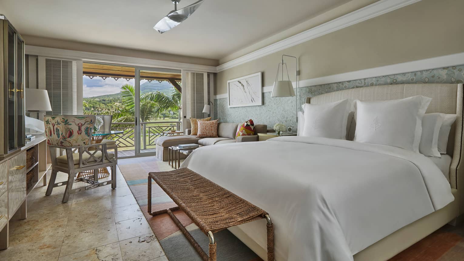 Nevis Peak View Room bed with white linens, wicker bench, sofa and chair, glass patio door