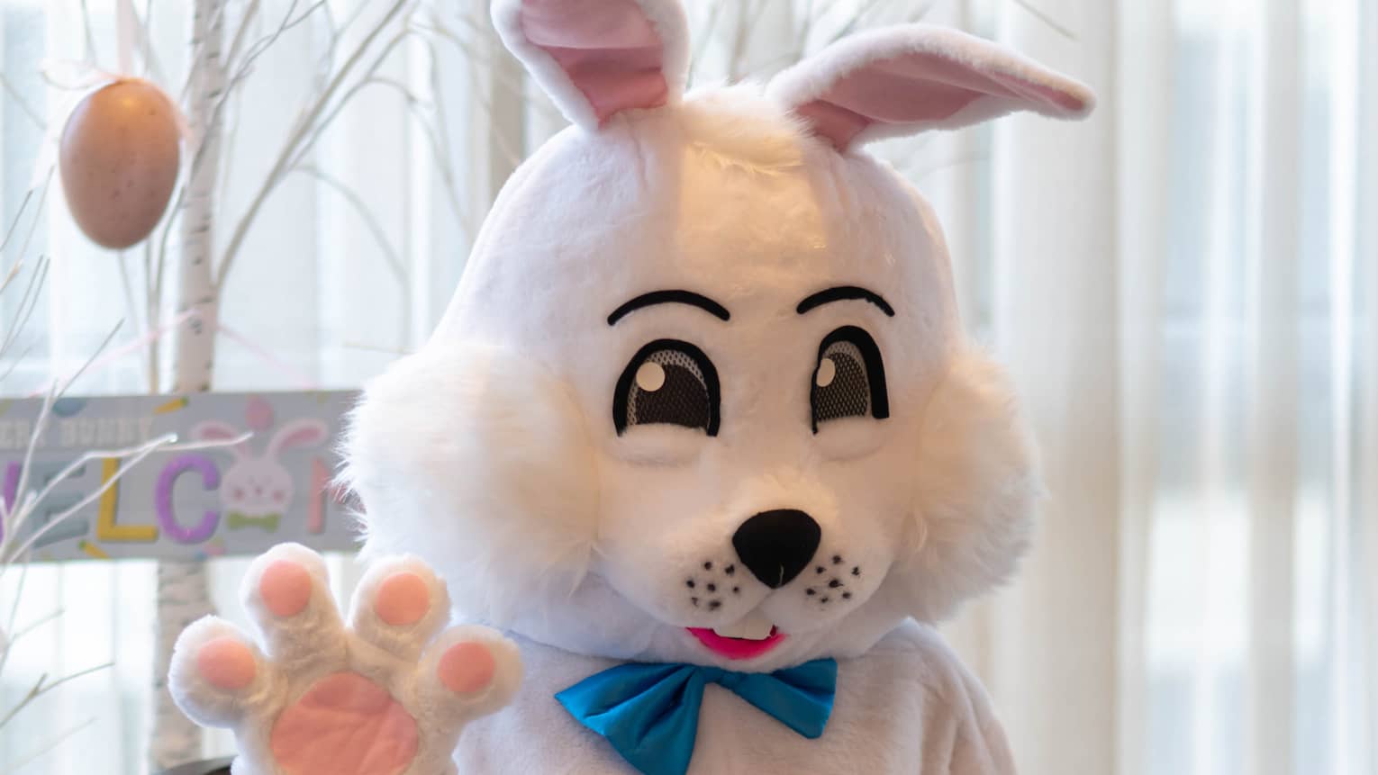 A person wearing an Easter Bunny costume and sitting near a tree decorated with Easter eggs