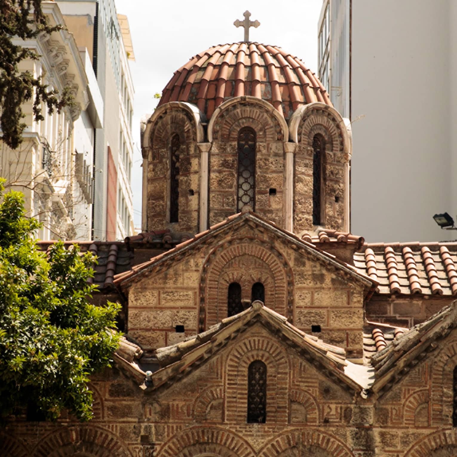 The dome of a church with narrow windows, carved arches, terracotta roof tiles and topped with an Orthodox cross.