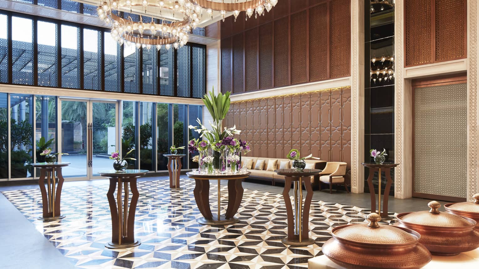 Spacious foyer with Art Deco style tile floors, cocktail tables under tall windows, round lantern chandeliers 