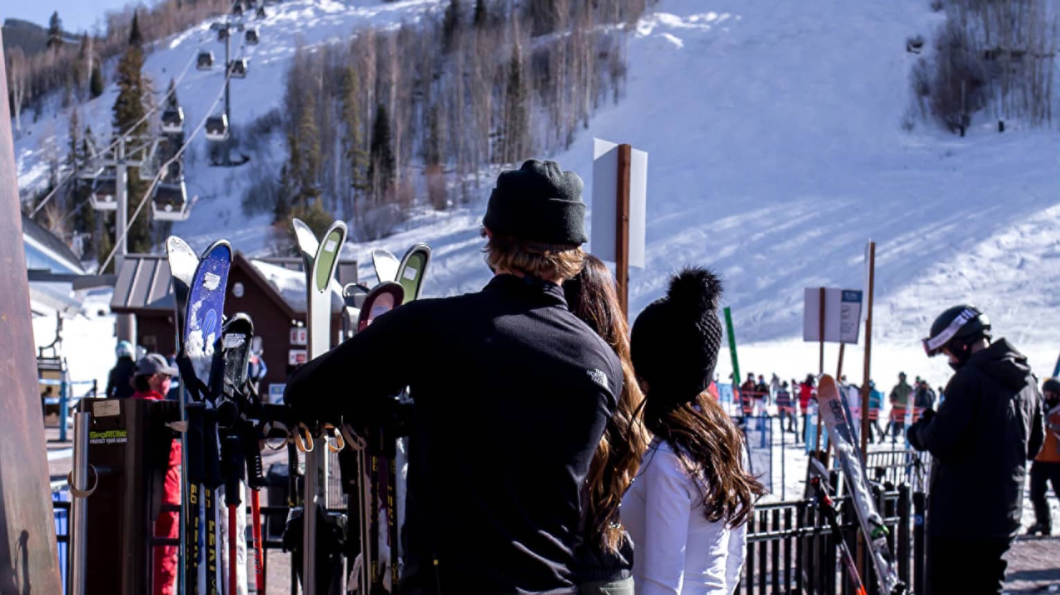 A group of people looking at skis and snowboards outside near a hill with snow on it.