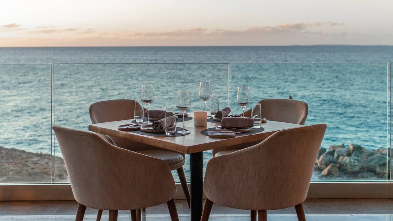 A private dining table set with wine glasses and plates on an outdoor terrace overlooking an ocean view