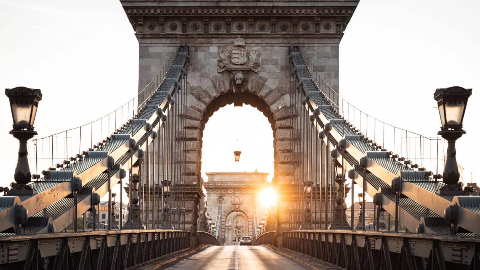 Driver's-eye view of an imposing stone bridge archway about to be passed under, a second further down, under the sun's glow.