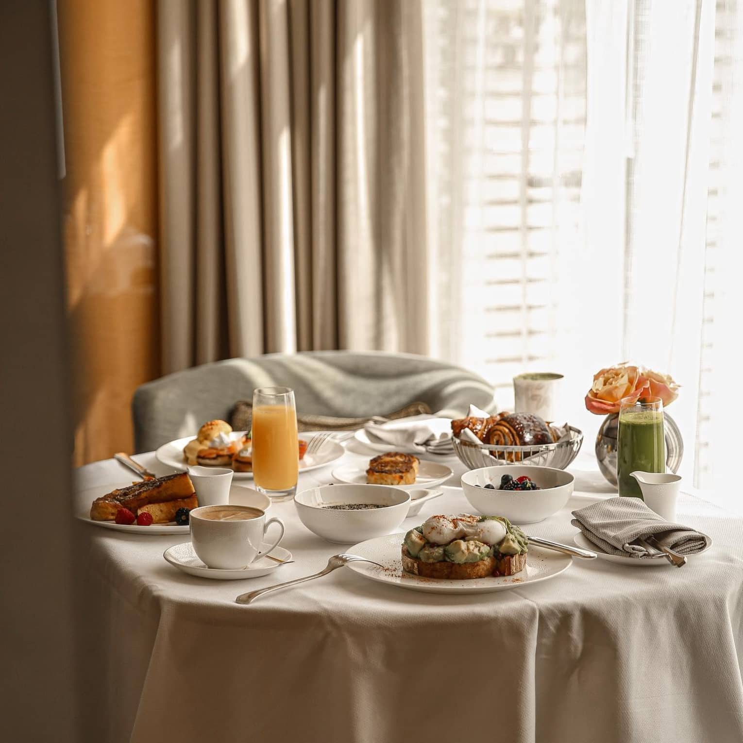 A circular table with a white linen tablecloth, filled with various breakfast meals and pastries, juice and coffee