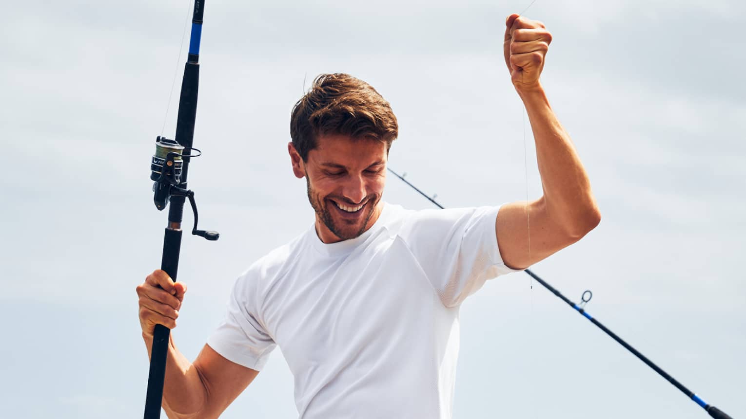 A man near the ocean holding a fishing line with a fish caught on it.