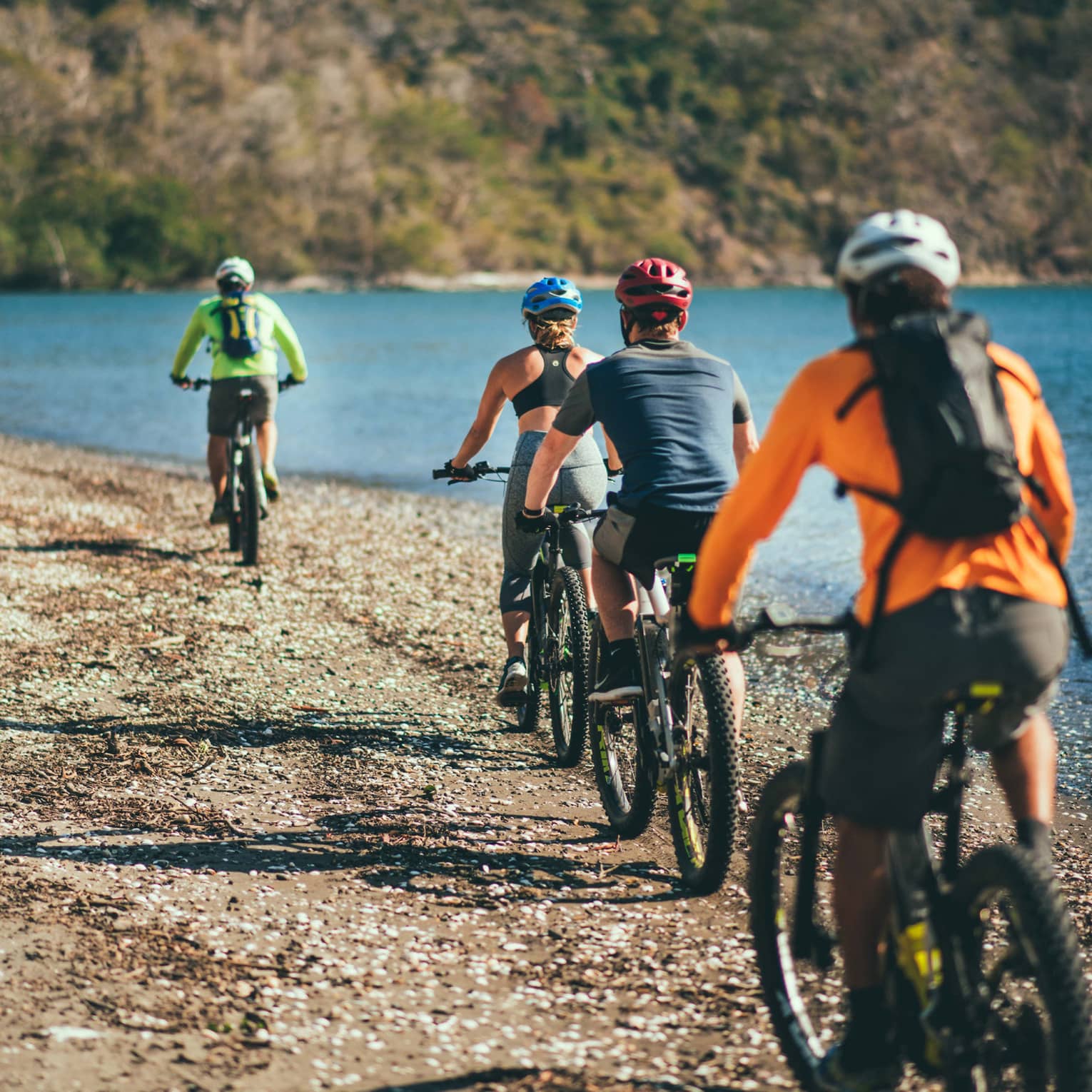 Four people riding bicycles through a rocky terrain next to the ocean