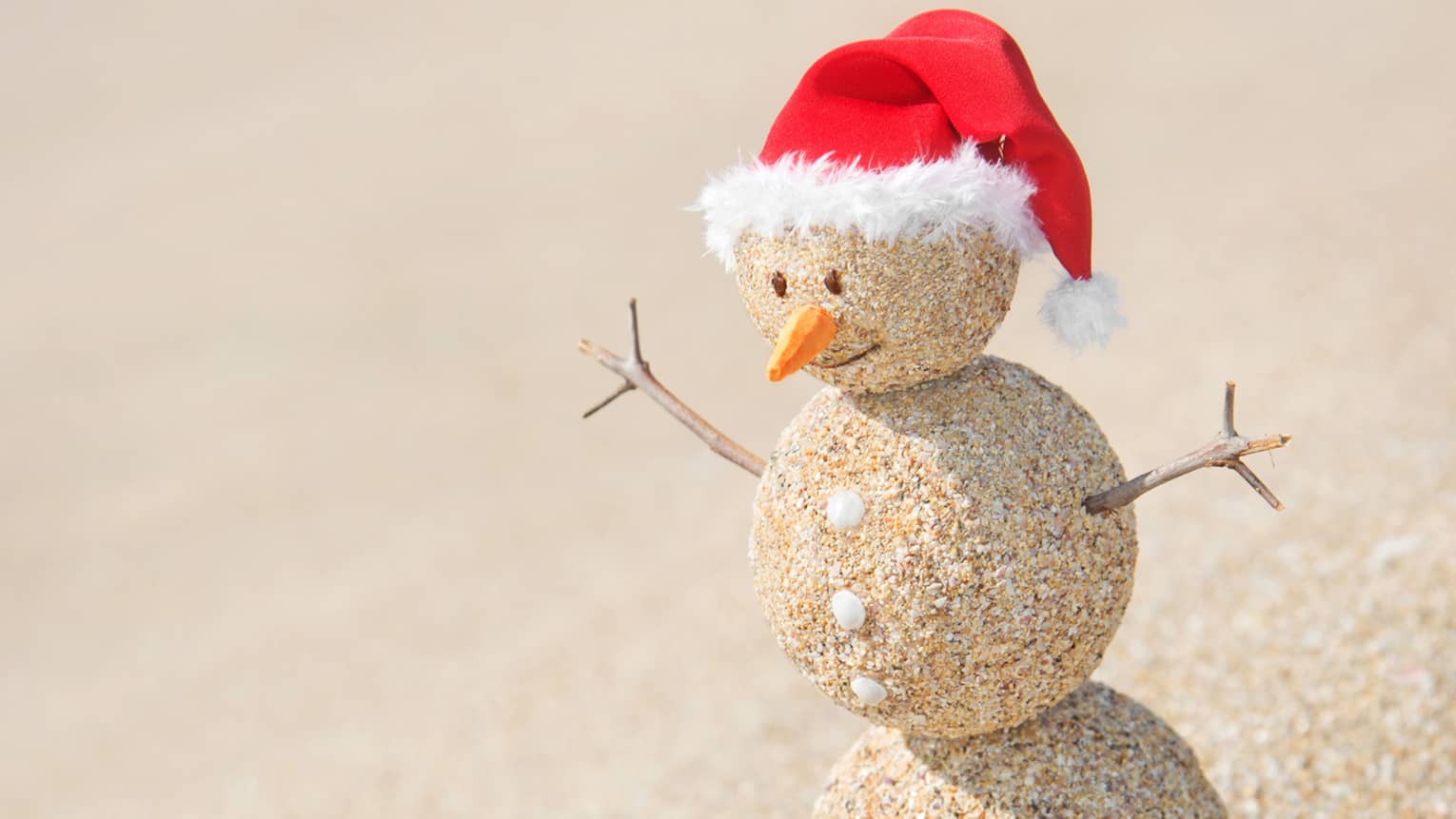 A snowman made out of sand with a red Santa hat.