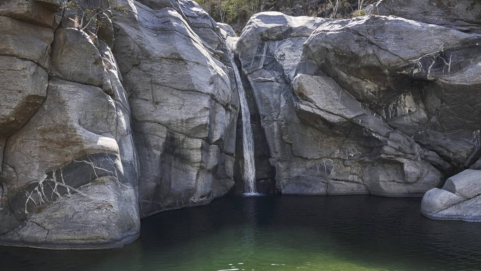 A person in a small well of water surrounded by large rock faces and trees.