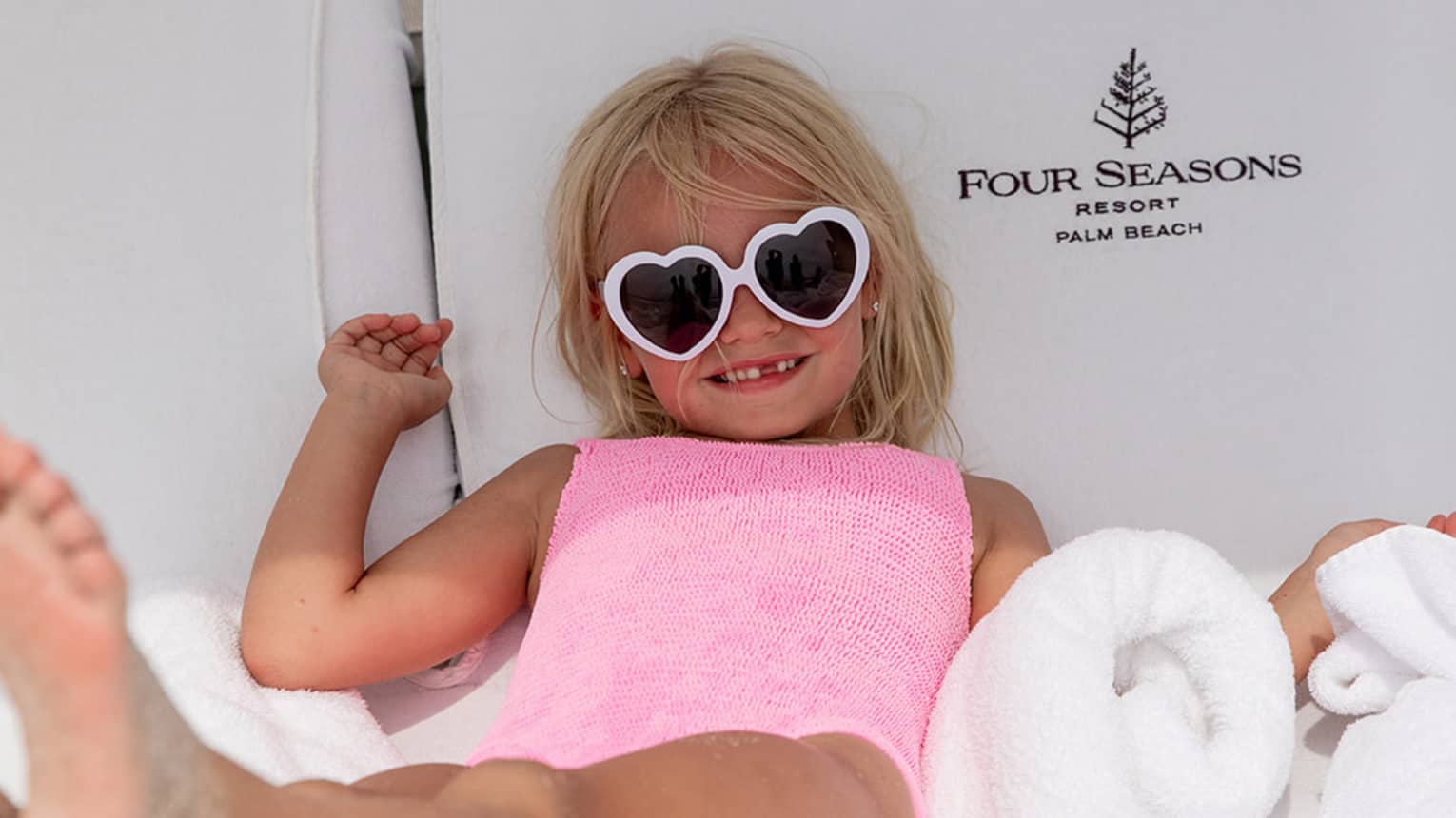 Young guest wearing heart-shaped sunglasses laying on a lounge chair.