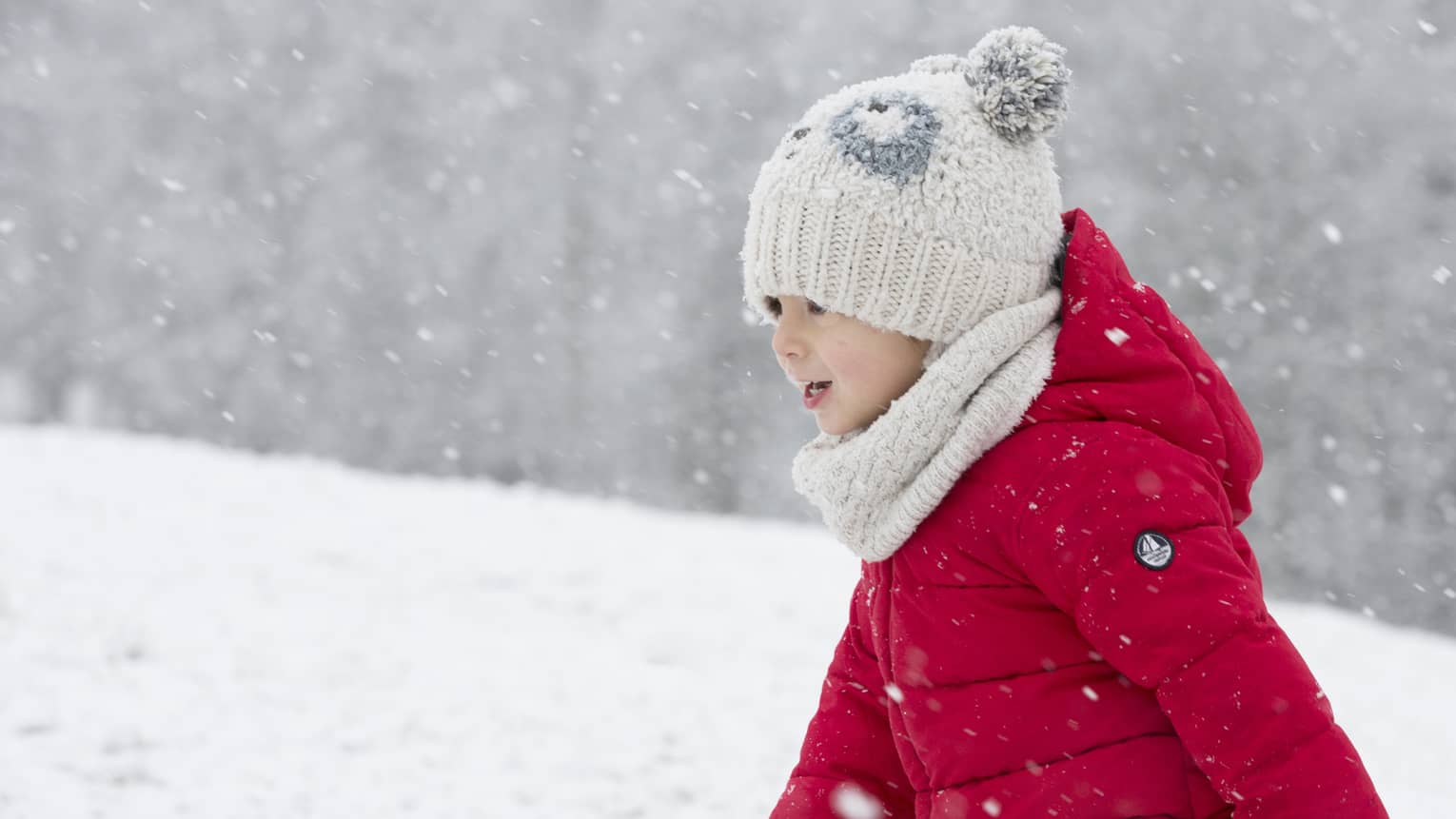 Child wearing red snowsuit and white hat playing in snow