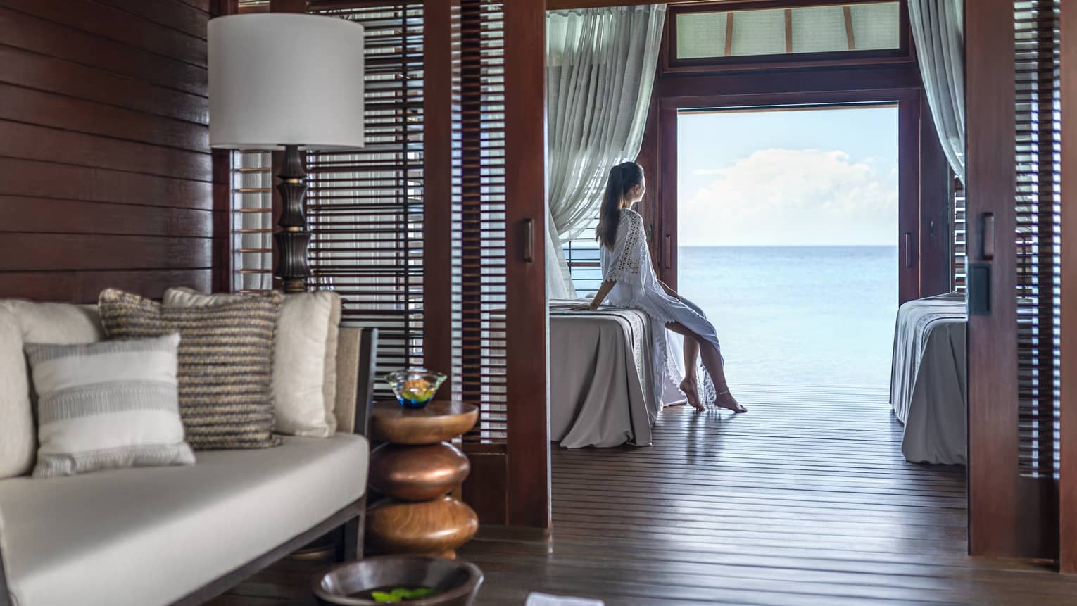 Person sitting on a massage bed in a serene spa treatment room with ocean view, surrounded by cozy seating and wooden décor
