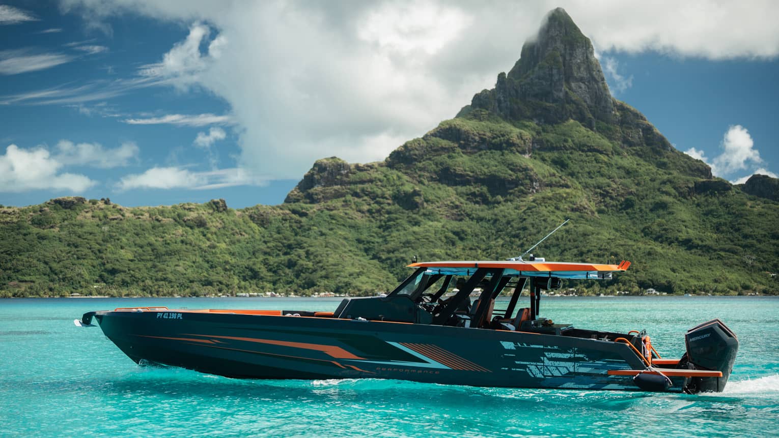 An orange and black yacht charter boar sails in front of a mountain landscape