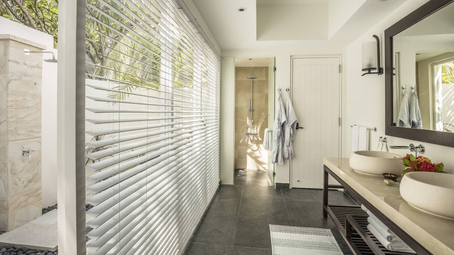 Bathroom of a two-bedroom bungalow with dual sinks, large mirror, a walk-in shower and floor-to-ceiling blinds offering a view of an outdoor shower area