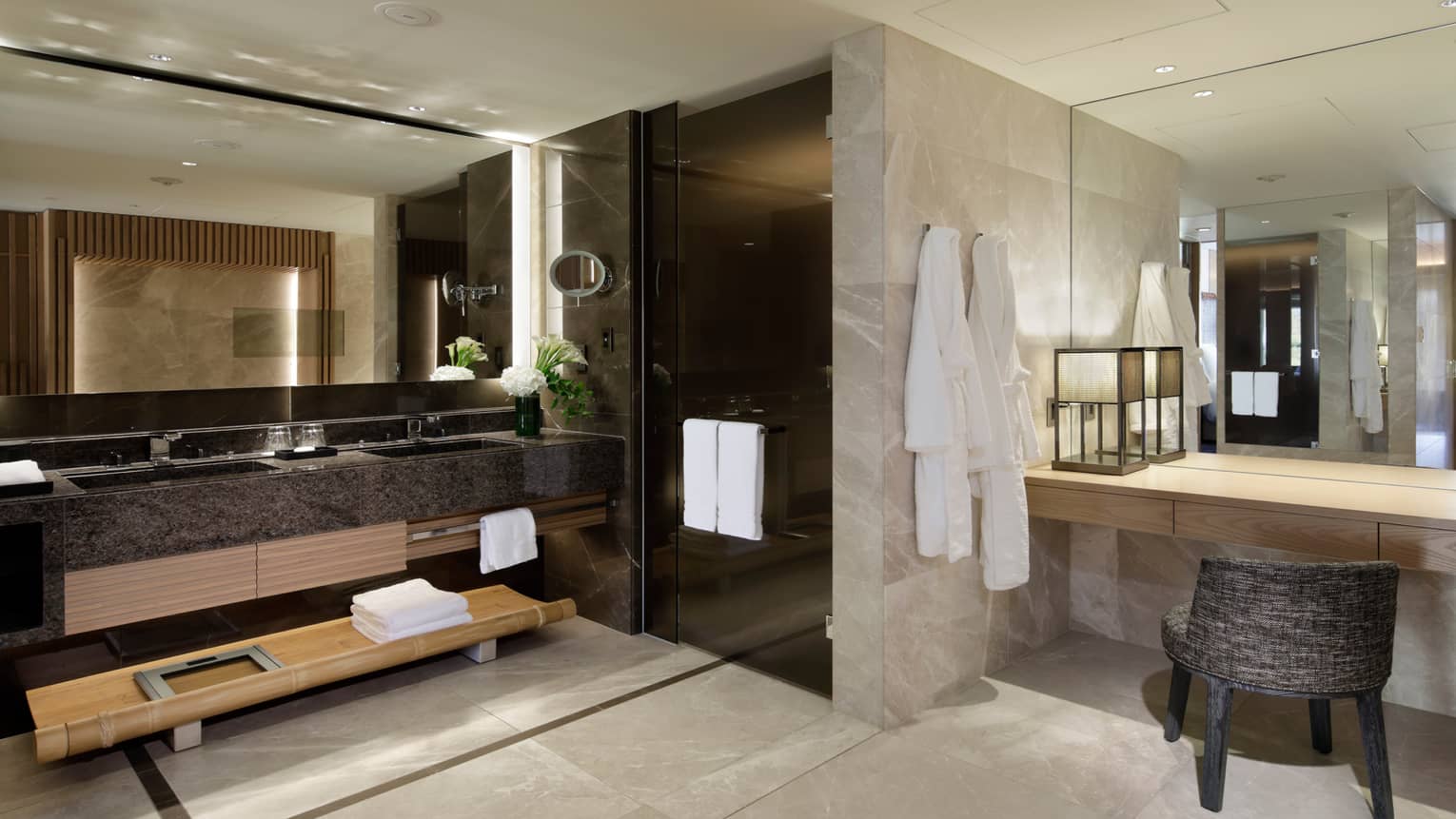 Large marble bathroom with double sink by black glass walk-in shower, vanity and chair