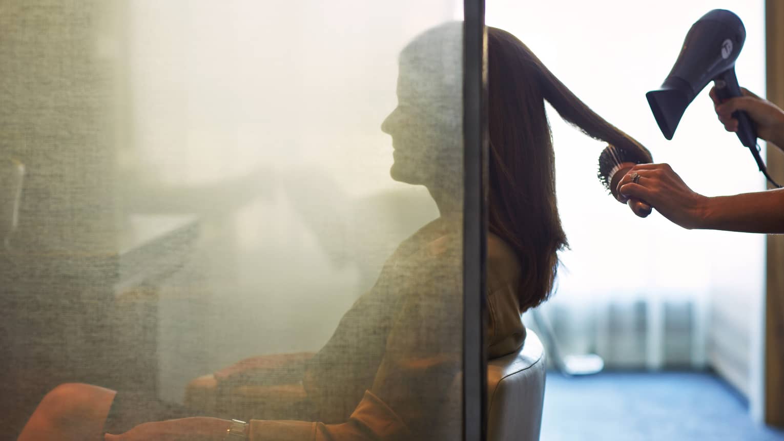 Silhouette of woman behind salon screen as hairdressers brushes, blow dries hair