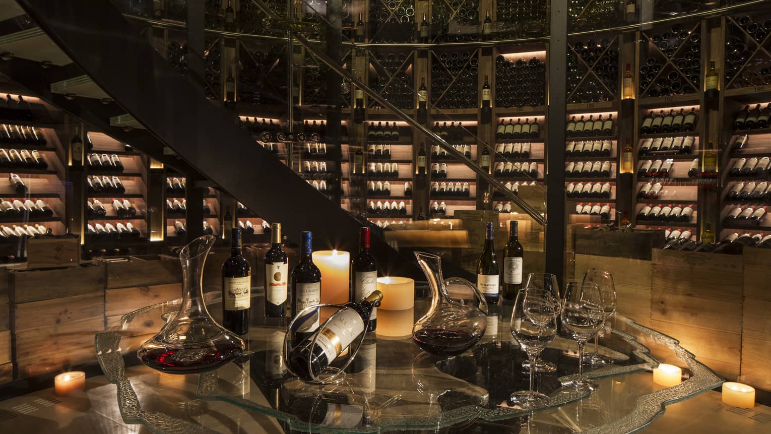 Bottles of wine are arranged for a tasting within an expansive, candlelit wine cellar