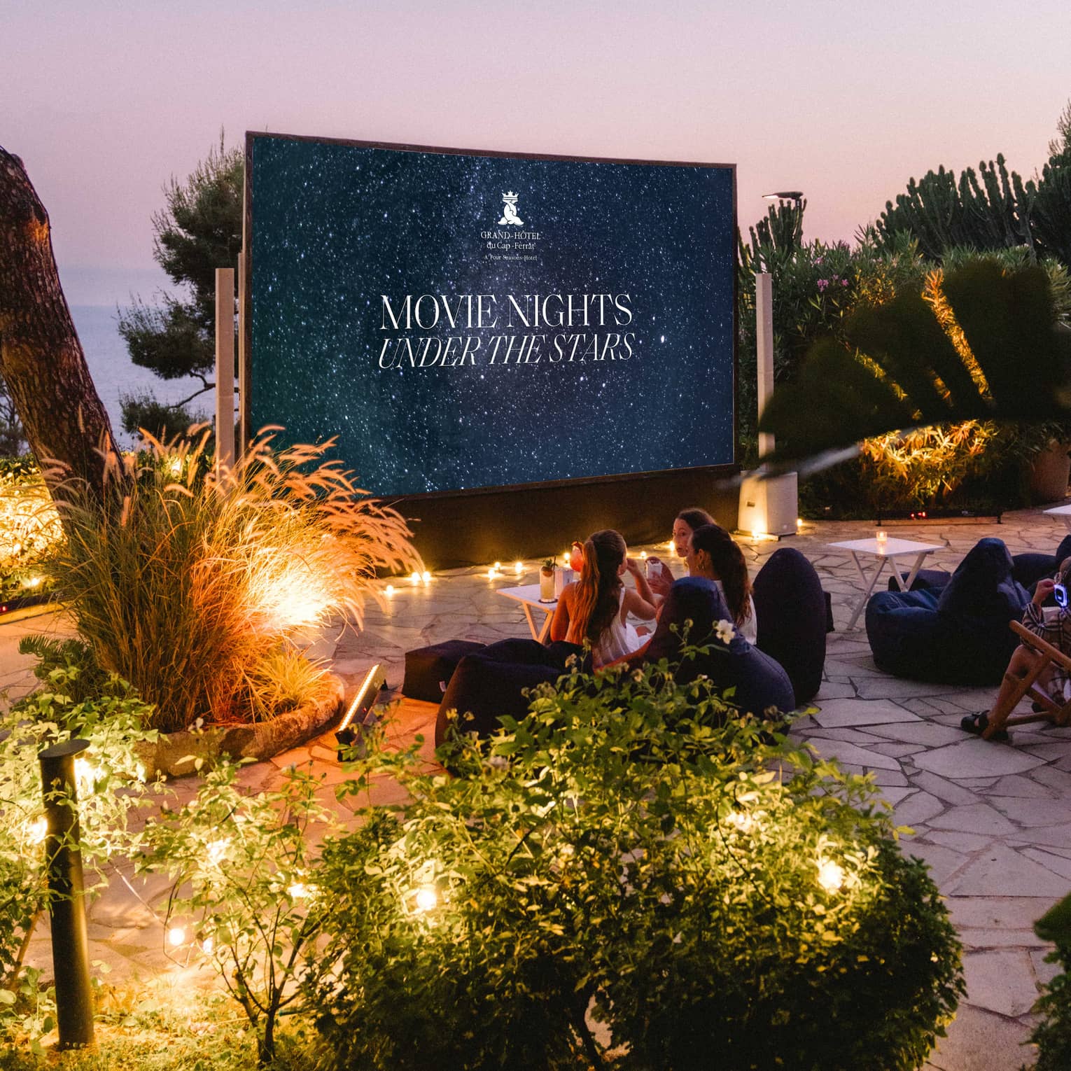 Families sit in front of a large outdoor movie screen