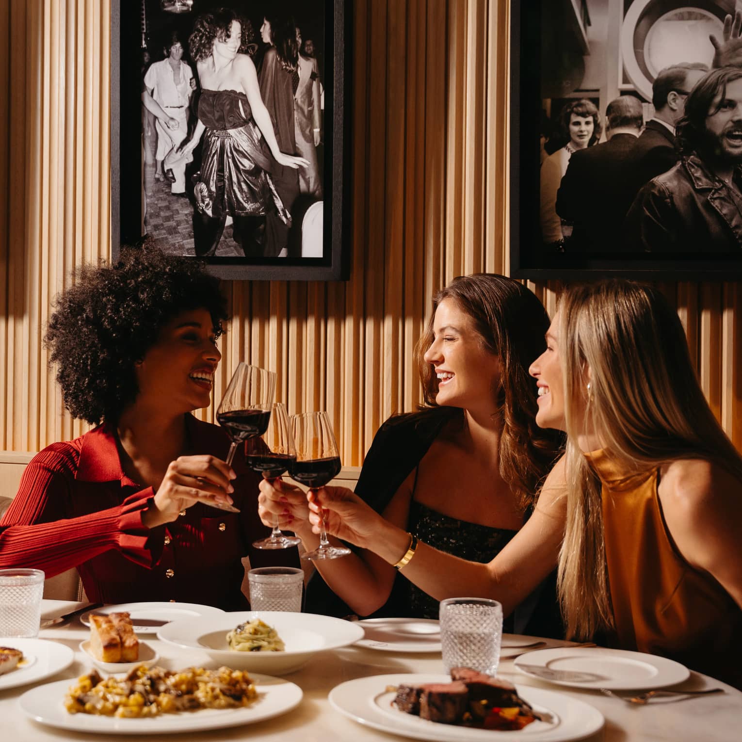 Three people sit around a restaurant dining table smiling and toasting their glasses together