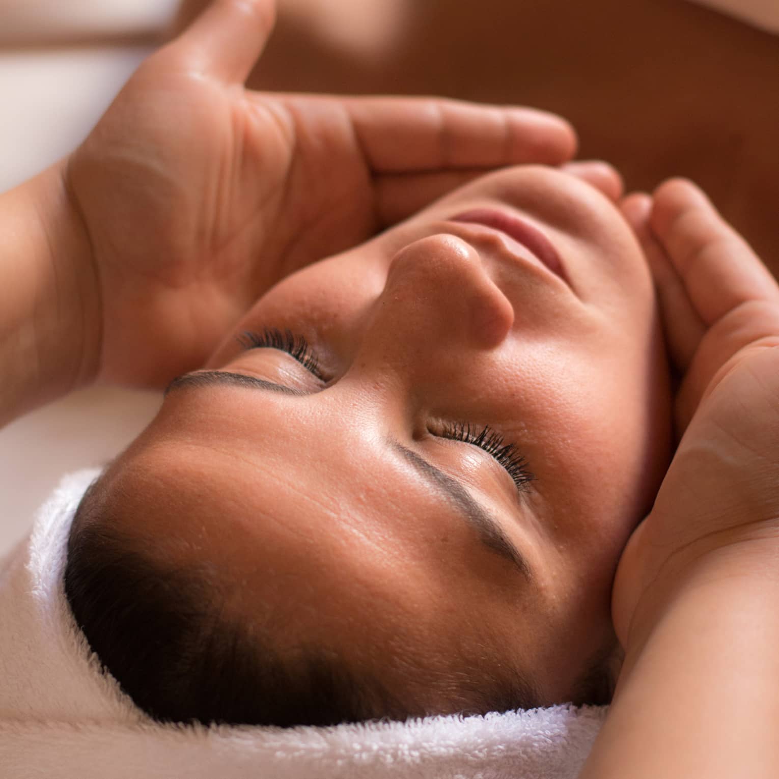 Close-up of woman with eyes closed facing up as hands cup her face and chin