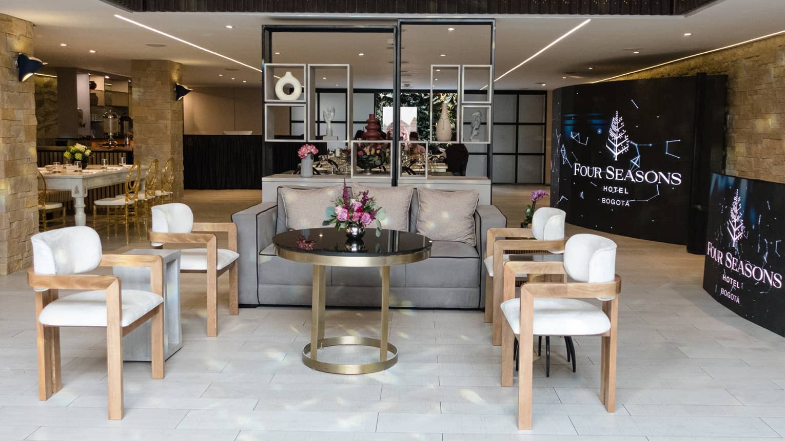 Meeting room with four arm chairs, a grey sofa, central round table and more seating in the background along with two large screens
