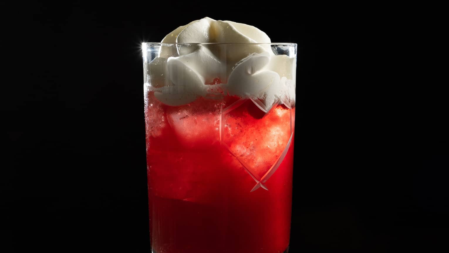 A deep red cocktail in a tall tumbler, with ice and white topping