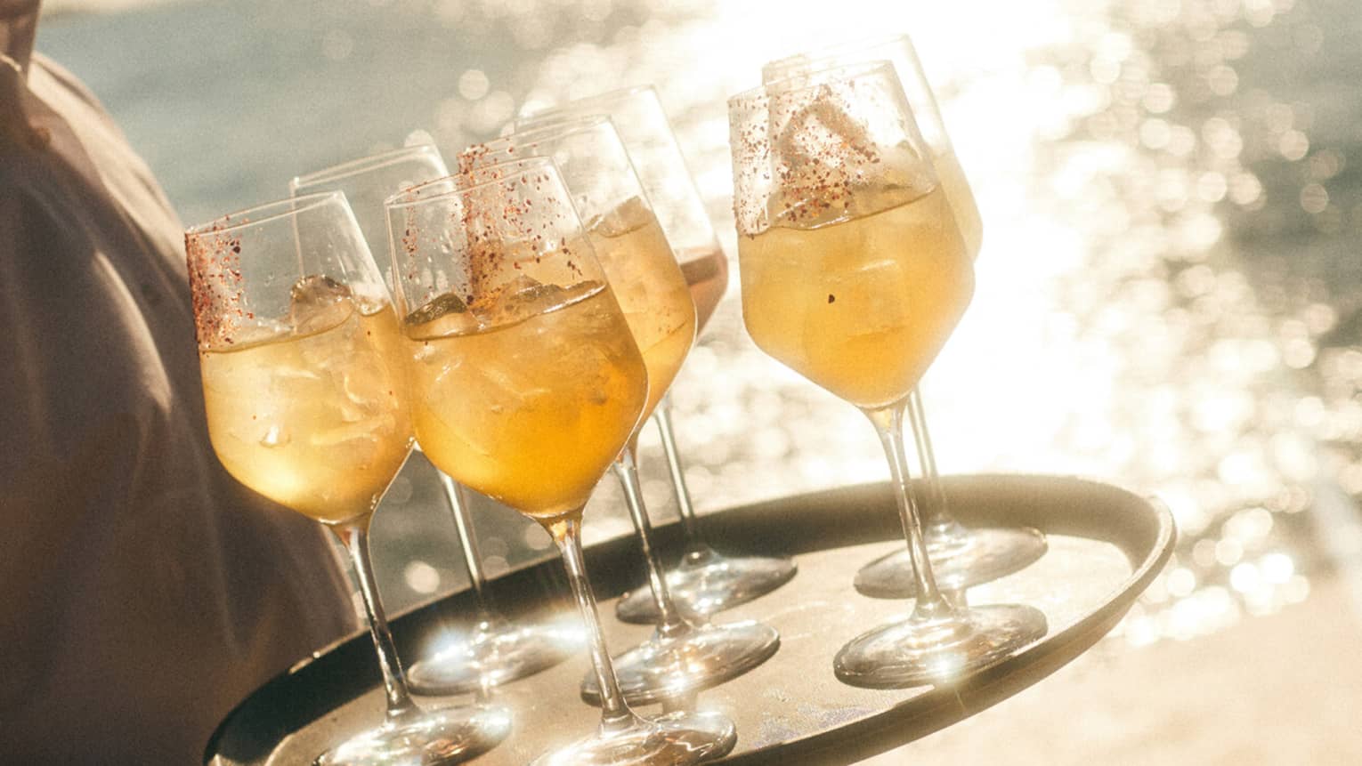 A server holds a tray of orange cocktails on a sunny beach