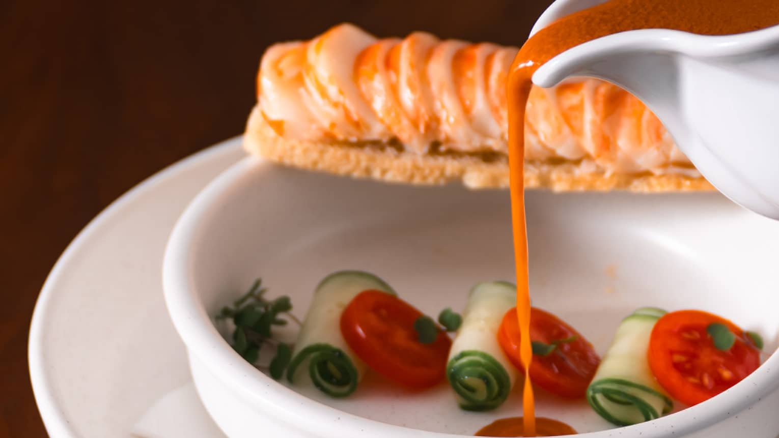 Lobster soup being poured into bowl with tomatoes and greens.