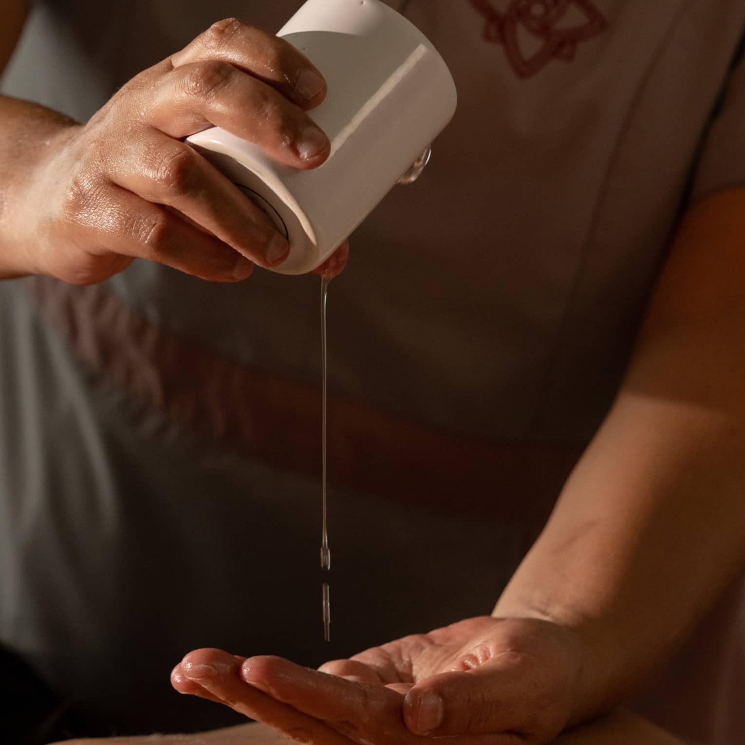A spa practitioner pours oil into their hands in a massage treatment setting.