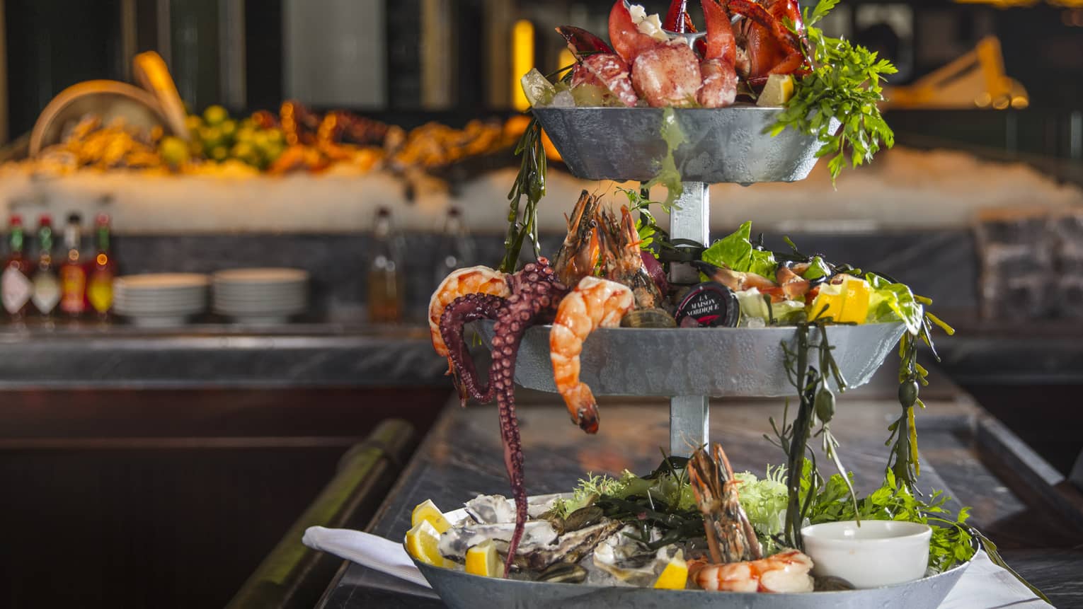 Three-tiered silver Grand Seafood Tower with shrimp, octopus, lobster claws, fresh lemon