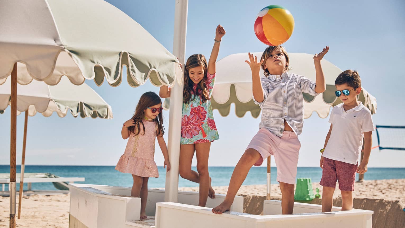 Four children playing on a sunny beach underneath white umbrellas