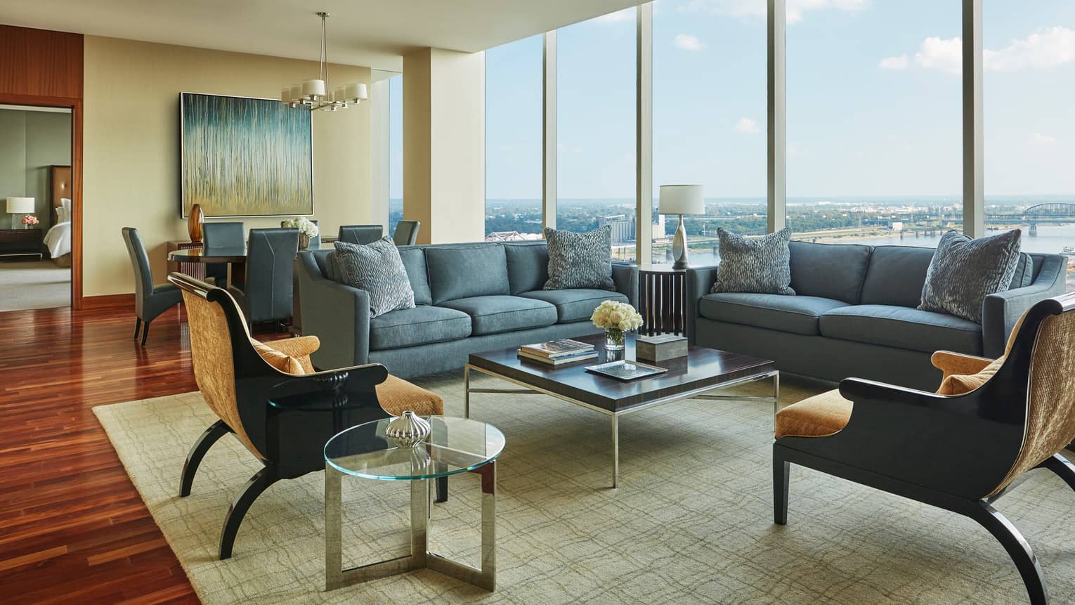 Large hotel room living area with two blue sofas, gold velvet armchairs and square coffee table