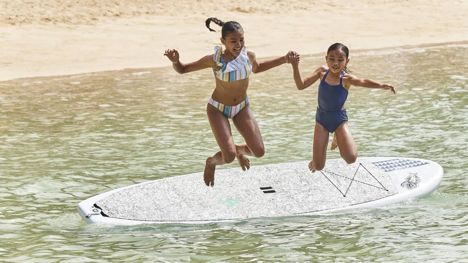 Two young girls jump hand-in-hand into the water from a stand-up paddleboard