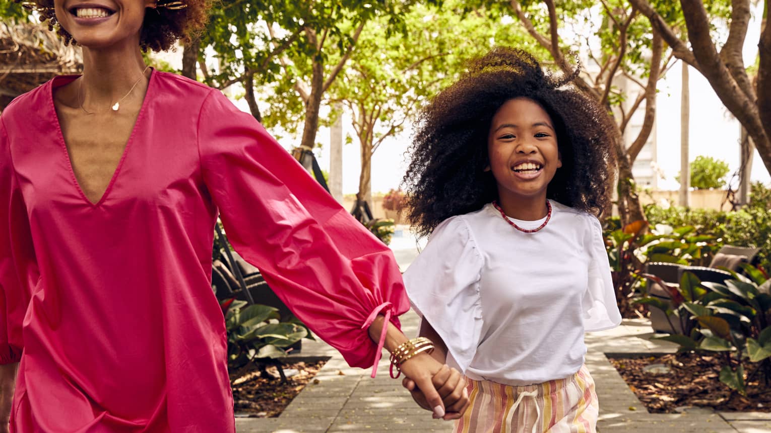 Woman and young girl walk hand in hand on sidewalk