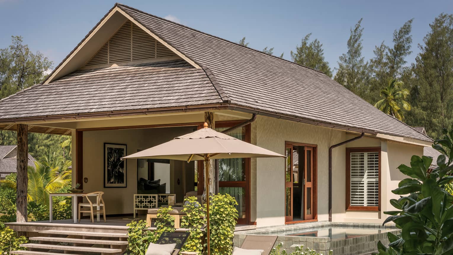 Exterior view of bungalow villa with two patio lounge chairs, umbrellas on lawn