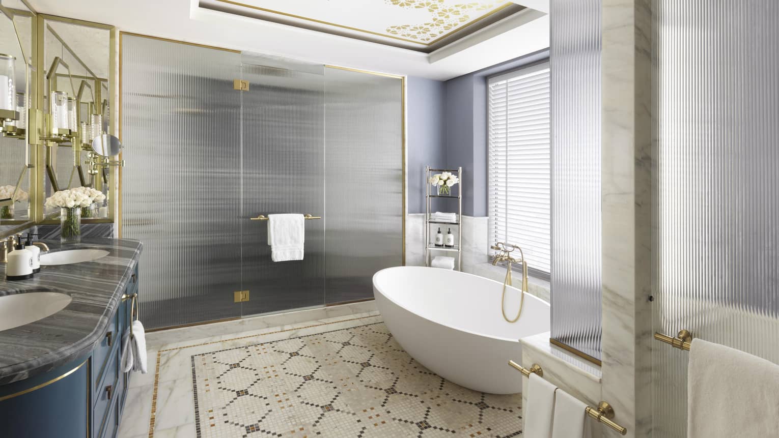 Royal Suite bathroom featuring patterned tile flooring, a white stand-alone bathtub, double vanity, large shower and gold fixtures