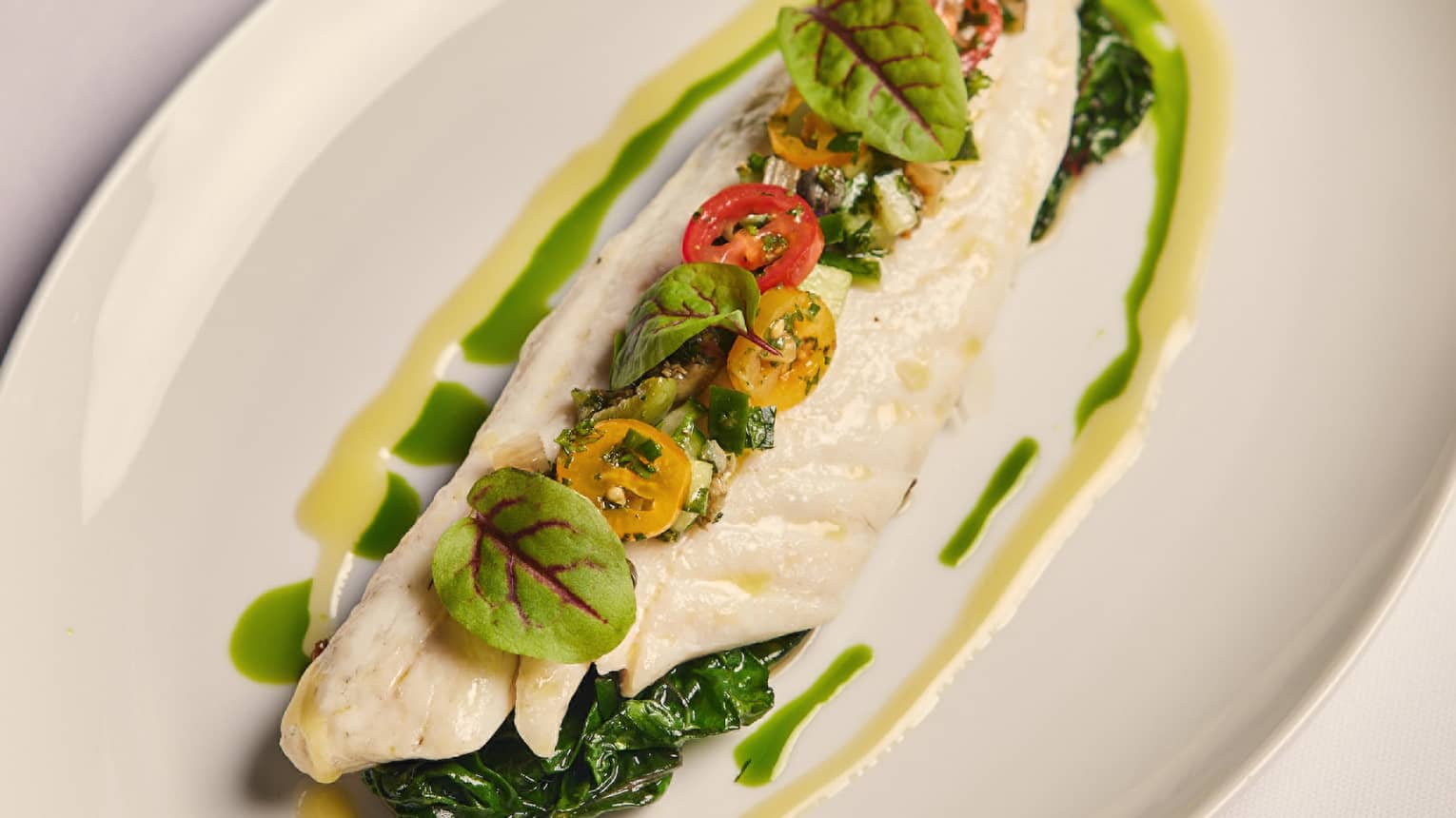 A fish dish on a green sauce with herbs and tomatos.