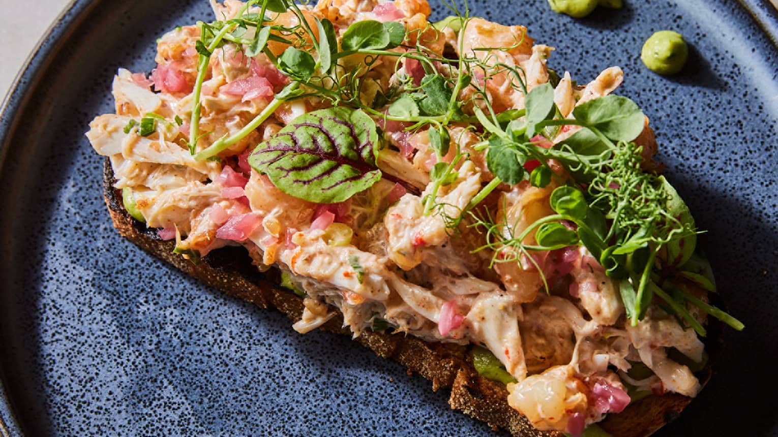 A round black plate holds a colorful food item with garnishes