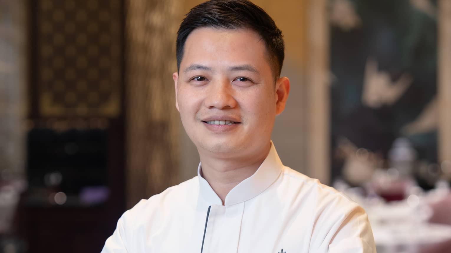 Smiling Asian man with arms crossed in white chef's jacket with Four Seasons logo