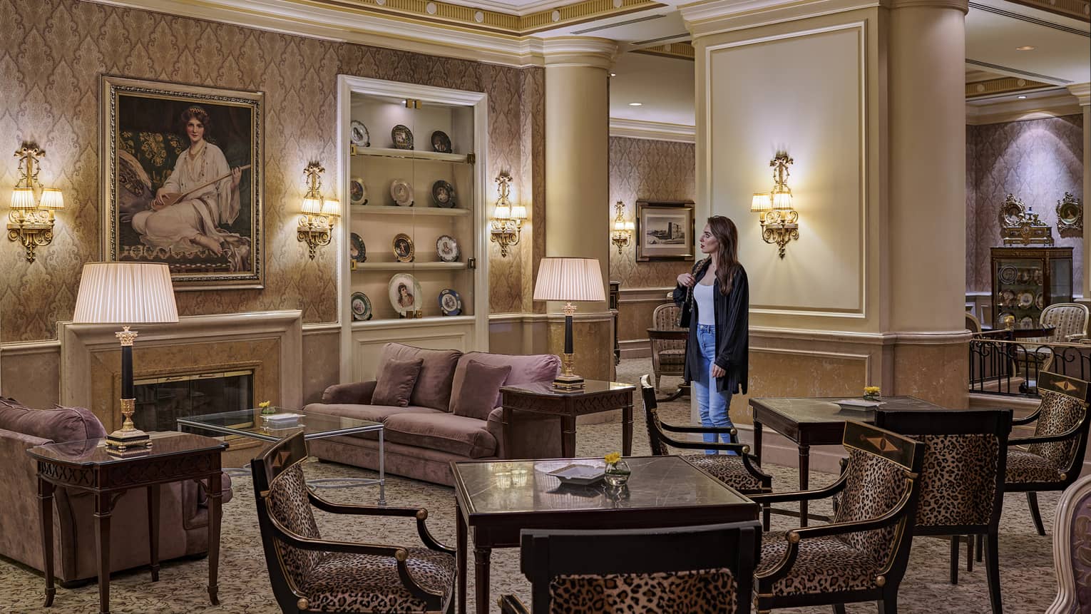 Woman stands in a lounge featuring two dark wood square tables, each with four chairs, two purple sofas