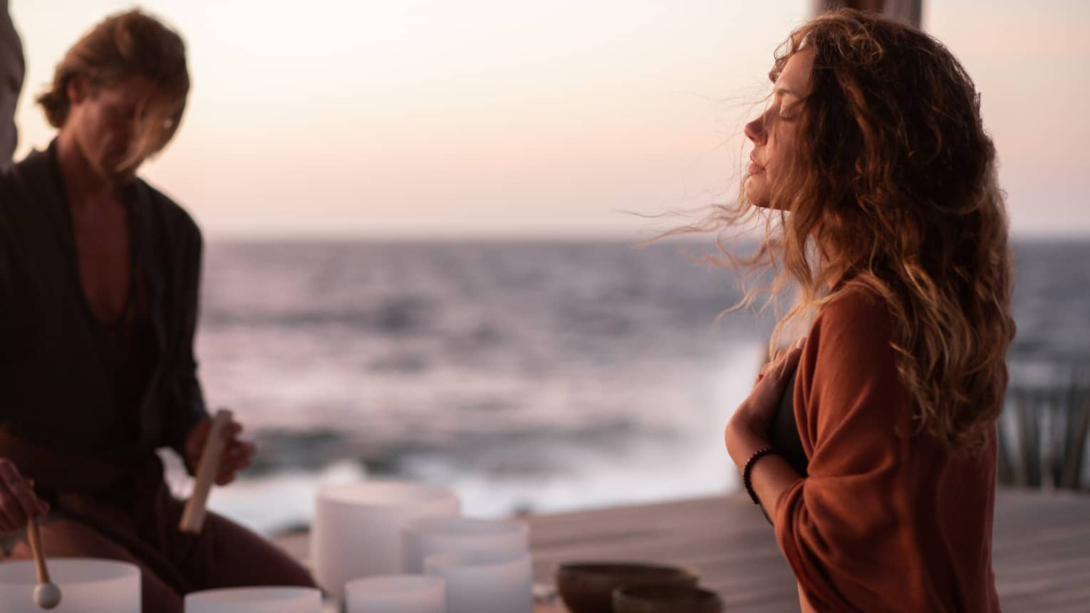 A woman participating in breathwork and sound meditation outside near an ocean.