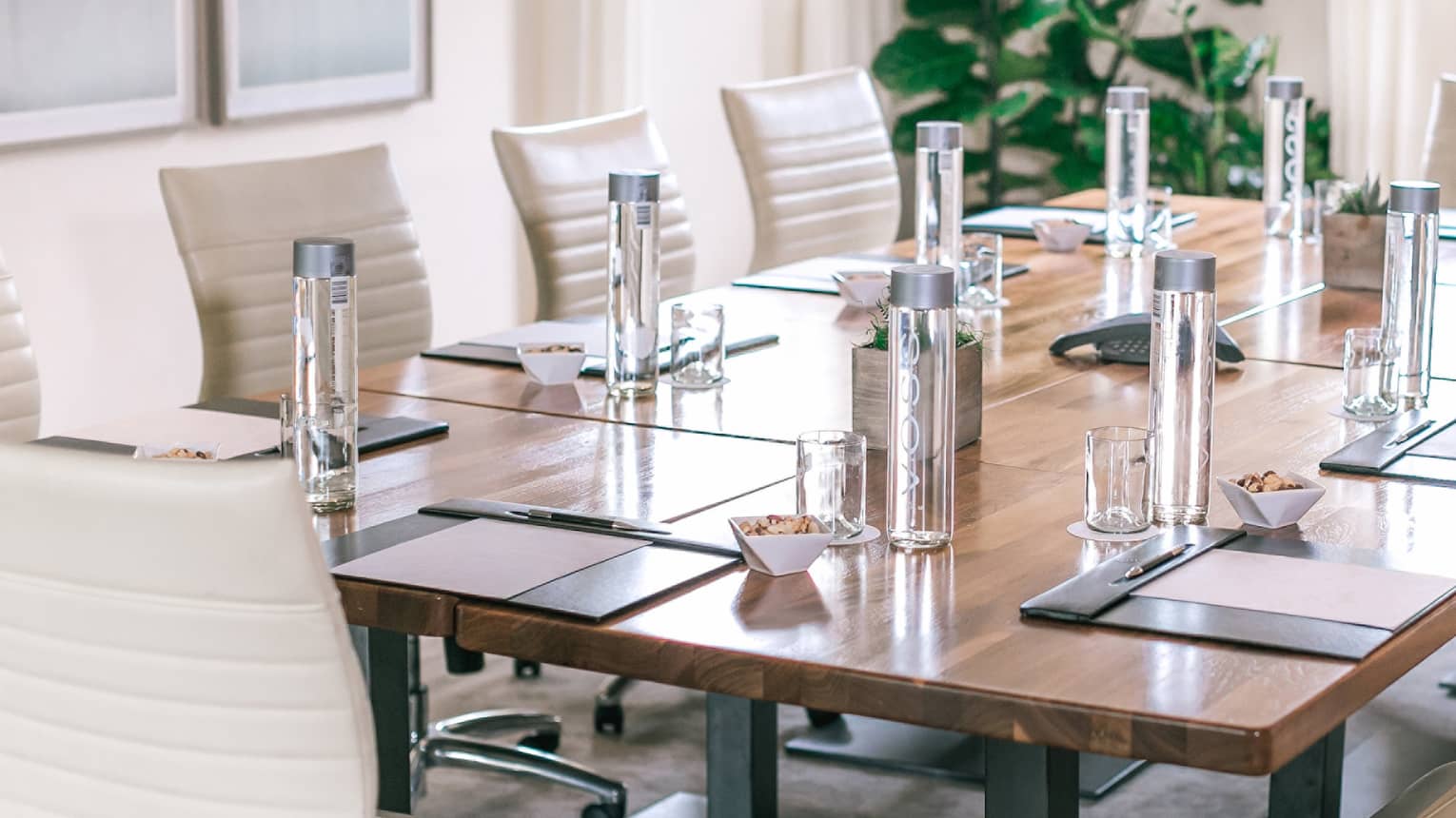 A rectangular boardroom table set with clear glass water bottles and black folders in a naturally-lit room