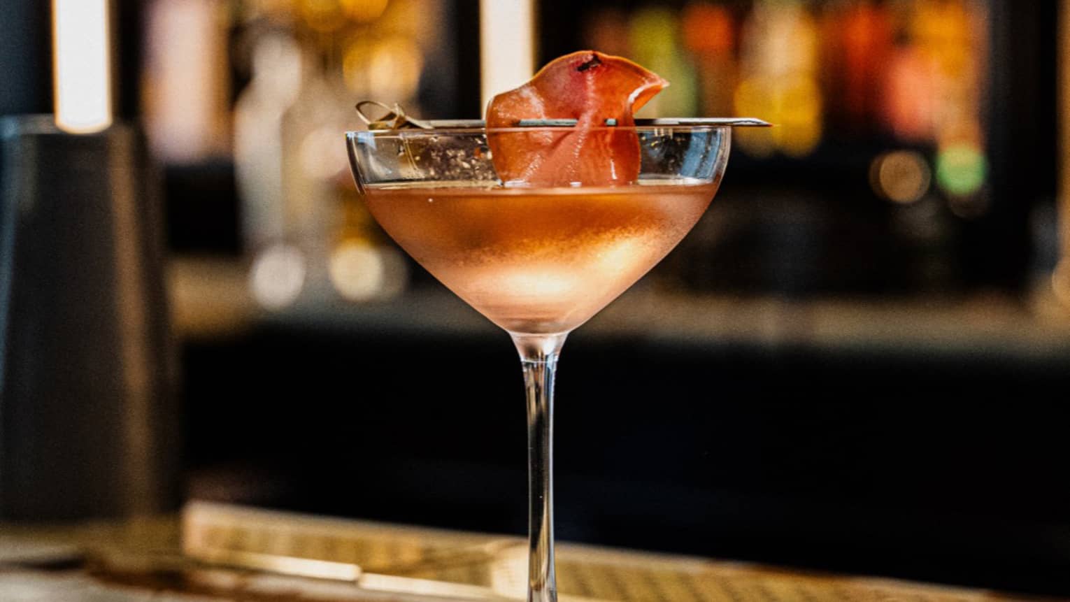 A light pinkish-orange cocktail in a stemmed glass