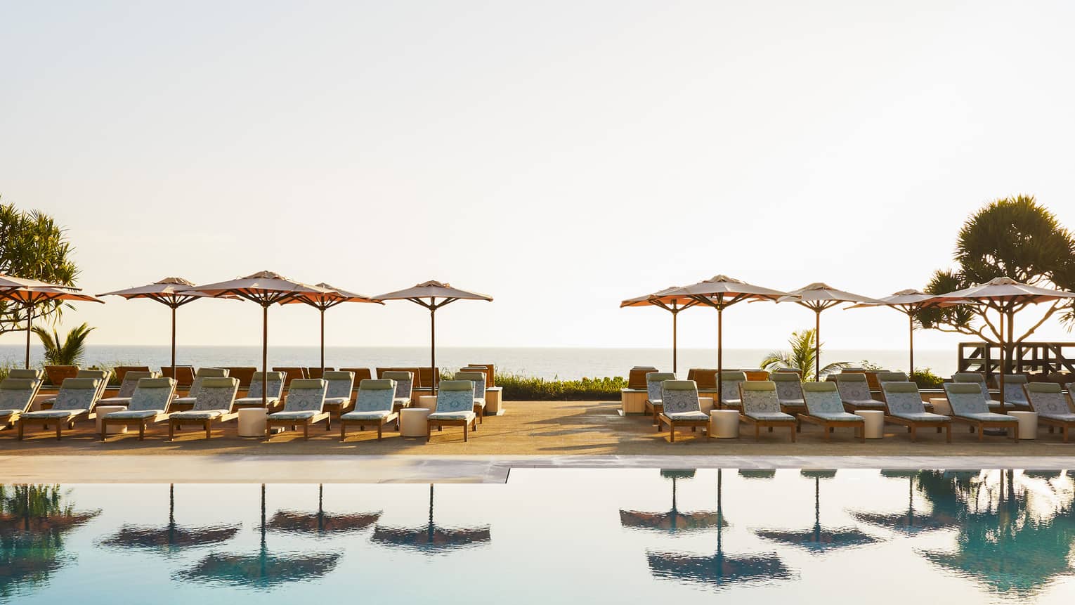 Rows of umbrellas and lounge chairs next to a pool outside.