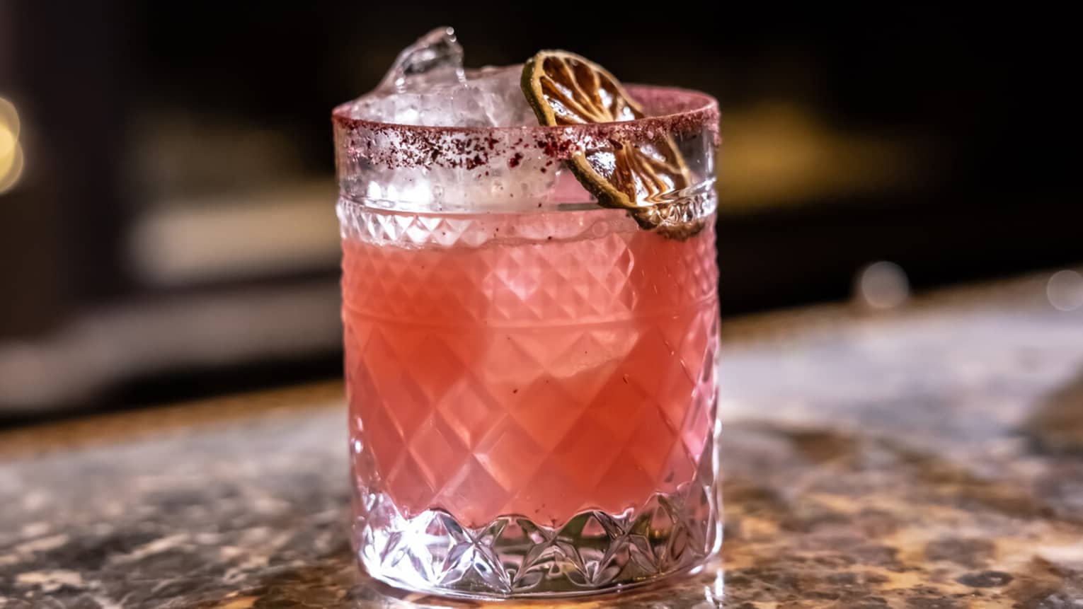 A pale pink cocktail garnished with dried citrus slice
