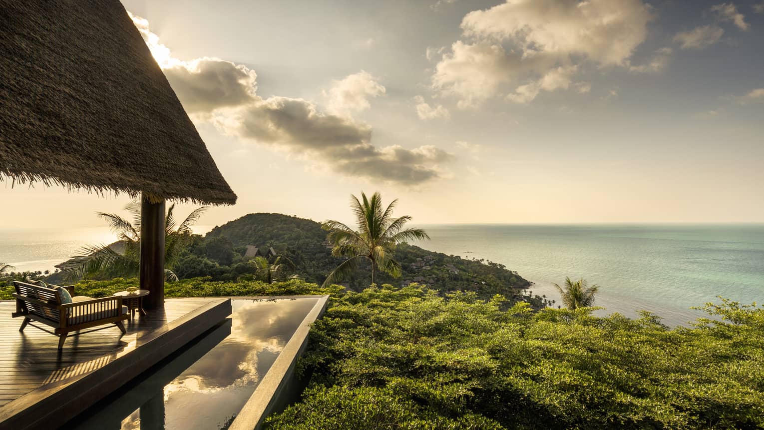 Patio lounge chair, thatched roof and deck overlooking canopy of tropical trees, ocean