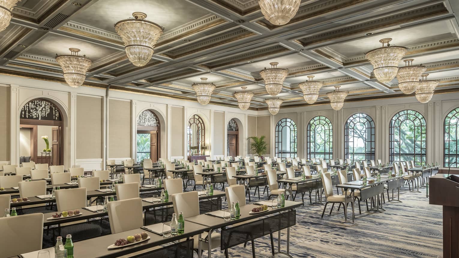 Bright, open ballroom with chandeliers and seats arranged facing forward, drinks and fruit on table