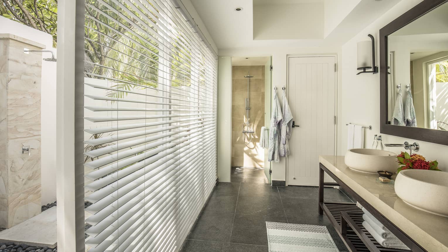 Bathroom of a two-bedroom bungalow with dual sinks, large mirror, a walk-in shower and floor-to-ceiling blinds offering a view of an outdoor shower area