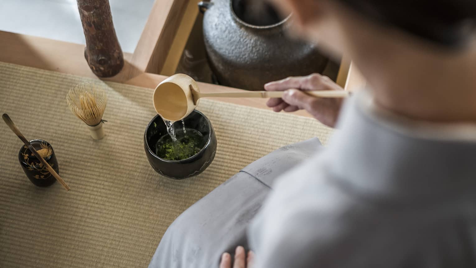 Woman kneels and pours tea from ladle during Tea Ceremony