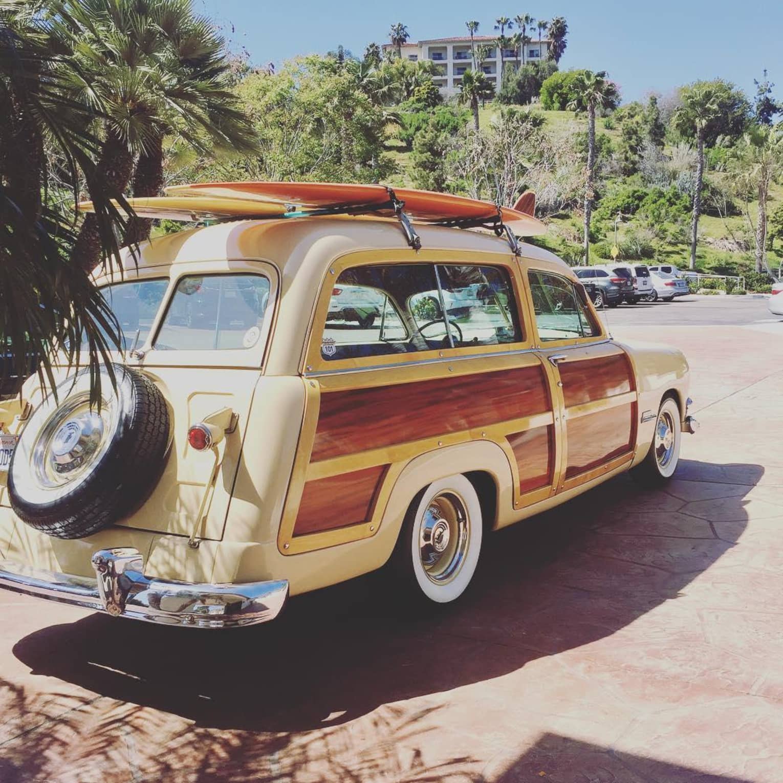 Wood-panelled 1951 Ford Woodie Station Wagon with surfboards strapped to top, in sunny parking lot